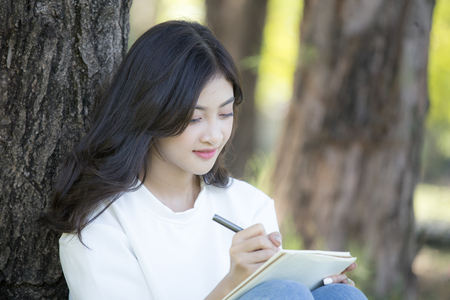 Asian Woman sketch picture on book with attractive smiling at garden. People lifestyle concept.の写真素材