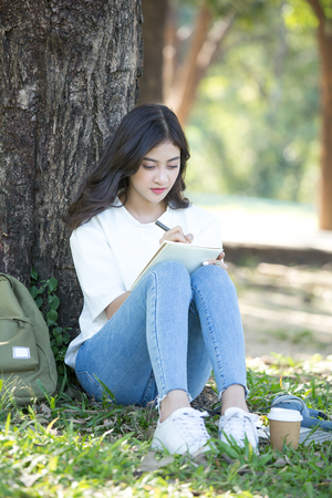 Asian Woman sketch picture on book with attractive smiling at garden. People lifestyle concept.の写真素材