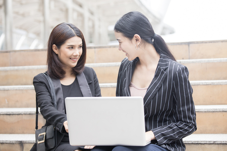 Beautiful woman sitting on a outdoors and using at laptop. Woman and friend having fun with new technology and shopping online at outdoor place.の写真素材