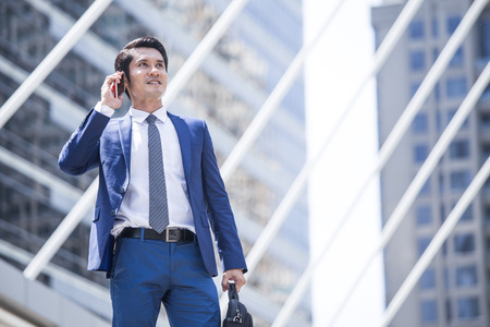Young Asian Businessman standing in City looking and use Smartphone for Work. Young Businessman have Confident for Work with Leader concept. Asian Businessman Thinking for Work in City.の写真素材