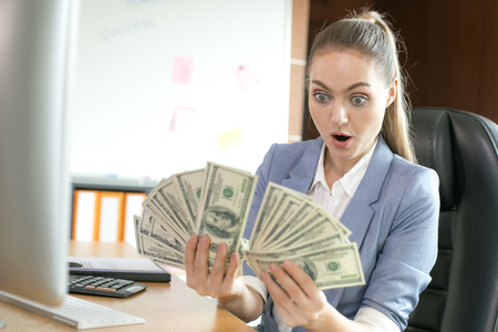 Young modern successful business woman holding a dollar at office. Woman success for online business.の写真素材