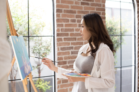 Asian woman paints picture on canvas with oil paints. Woman painting picture with attractive smiling.の写真素材