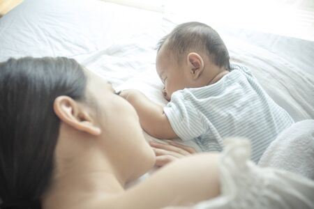 Mother and new born baby sleepling on a white bed together.