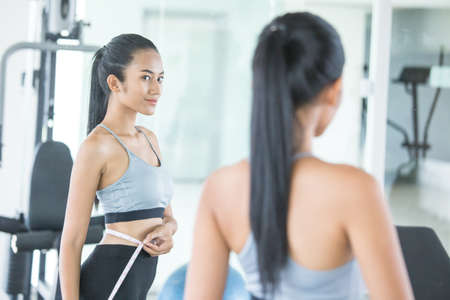 Asian beautiful woman looking her body mirror at gym. Sport and Reaction concept.の写真素材