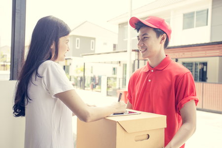 Young Delivery Man giving a Cardboard Box to Woman with Attractive smiling at Home. Delivery Concept. Vintage tone.の写真素材