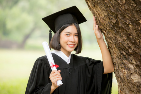 Young Asian Woman Students wearing Graduation hat and gown, Garden background, Woman with Graduation Concept.の写真素材