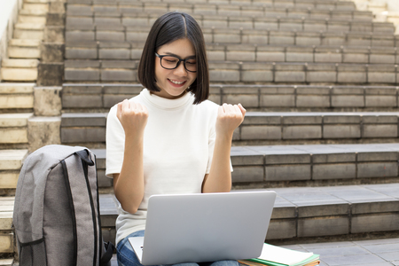 Portrait of Attractive Asian Student Woman sitting at outdoor place. Woman using laptop with Attractive Smiling to Camera. People with Education Concept.の写真素材