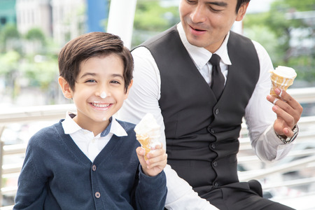 Father and Son Eating Ice Cream Together with Attractive Smile. Boy looking to Camera while Eating Ice Cream with Happy Emotion.の写真素材