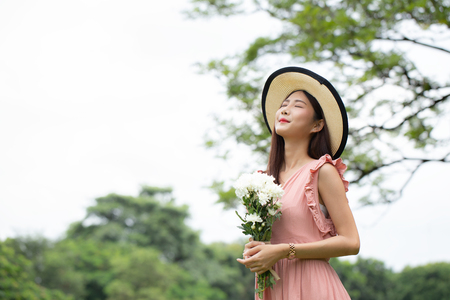 Asian attractive woman carrying flower in hand with relax emotion at garden. Women resting at garden in holiday. People with lifestyle, relax, summer, holiday concept.の写真素材