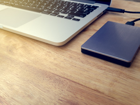 External or portable hard drive (HDD) connected to laptop computer for transfer or backup data on wooden texture office desktop with copy spaceの写真素材