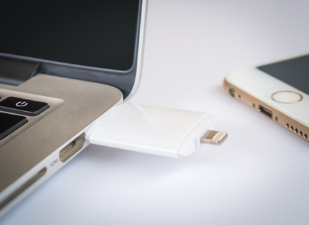 CHINGRAI, THAILAND -SEPTEMBER 7, 2016: Close-up image of two way external flash storage transfering data with Apple Macbook Pro Retina and close to Apple iPhone 6 on white background.のeditorial素材