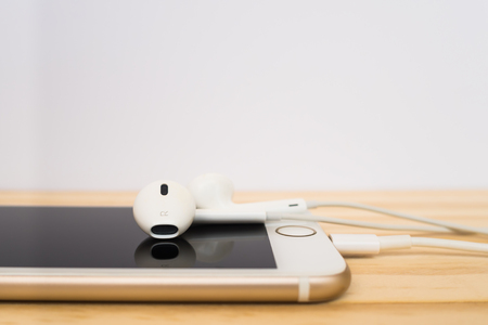 CHIANGRAI, THAILAND -SEPTEMBER 15, 2016: Side view of new Apple Lightning EarPods mockup on top of new Apple iPhone 7 mockup and reflection on screen on wooden table.のeditorial素材