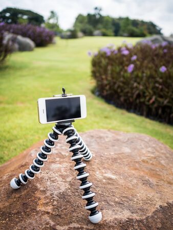 Smartphone installed on flexible tripod and preparing to take a photo or video on rock in the flower garden at Chiangrai, Thailand.の写真素材