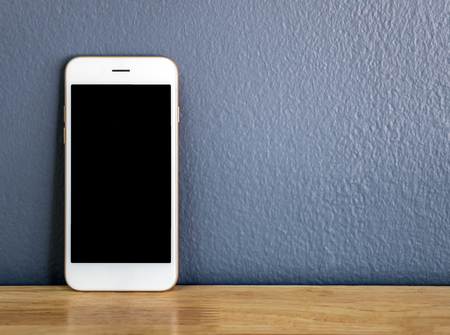 Front view image of white smartphone leaning against the gray wall on wooden table with copy space
の写真素材