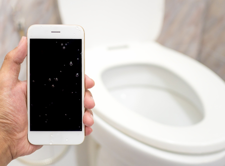 Human hand holding wet smart phone in water closet with copy space. Water damage, waterproof concept.の写真素材