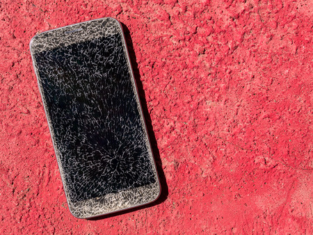 Top view and close-up image of old broken and cracked screen smartphone drop down on the red floor background with copy spaceの写真素材