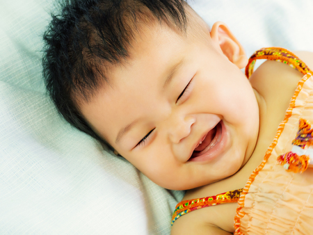 Portrait of cute short hair asia baby gril relaxing smiling or laughing and lying on her bedの写真素材