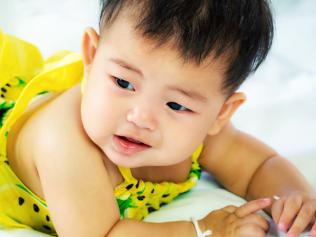 Portrait of cute short hair asia baby girl in color full wearing relaxing and crawling on her bedの写真素材