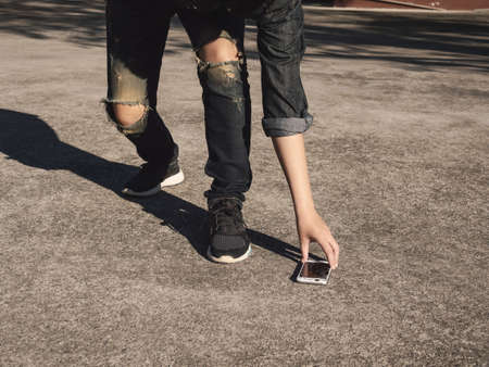 Young man picking broken and cracked screen smartphon from floor after dropped. Concept of broken or accident mobile phone, repair, warranty and technologyの写真素材