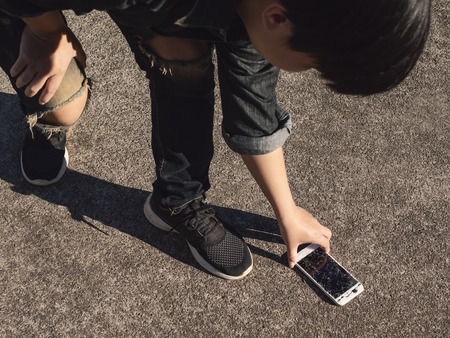 Young man picking broken and cracked screen smartphon from floor after dropped. Concept of broken or accident mobile phone, repair, warranty and technologyのeditorial素材