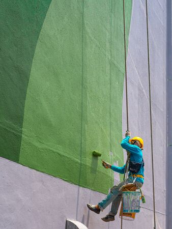 Chiang Rai, Thailand: September 18, 2019 - Two painters are painting the exterior of the building on a dangerous looking scaffolding hanging from a tall building.のeditorial素材