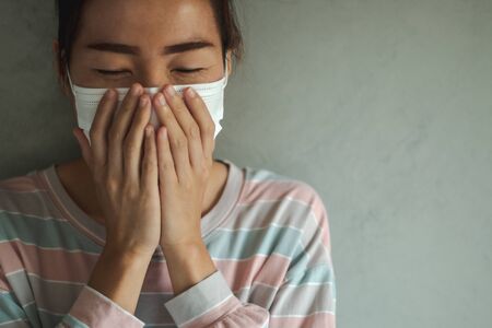 Beautiful Asian woman infected with the Coronavirus (COVID-19) sneezing in medical hygiene protective mask. Health care, quarantine and prevent from risk of Coronavirus (COVID-19) concept.の写真素材