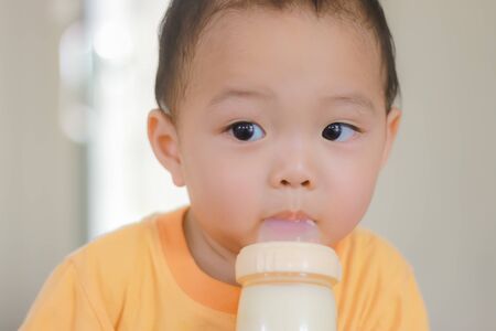 Close-up of Asian adorable toddler kid holding milk bottle in mouth. Baby care and childhood concept.の写真素材