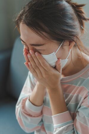 Beautiful Asian woman infected with the Coronavirus (COVID-19) sneezing in medical hygiene protective mask. Health care, quarantine and prevent from risk of Coronavirus (COVID-19) concept.の写真素材