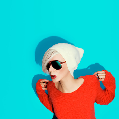 fashion blond girl with trendy hat and sunglasses on a blue backgroundの写真素材