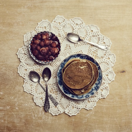 Pancakes with jam and spoon on the old patterned napkins on wooden table