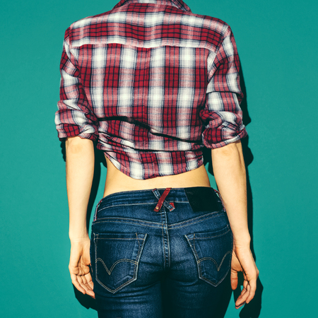 model girl in checkered shirt and blue jeans on green background from the back