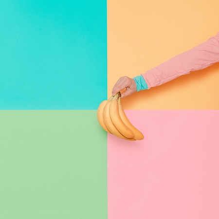 Hand in fashionable clothes holding Bananas. Vanilla summer style Minimal creative artの写真素材