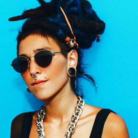 Fashion Spanish Girl with dreadlocks and stylish accessories on the blue wall.