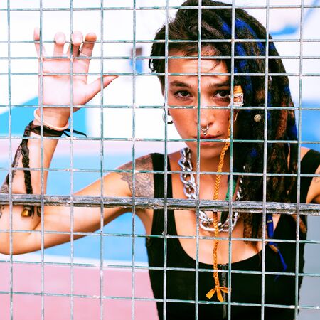 Girl with dreadlocks behind the metal grid on sports groundの写真素材