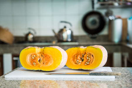 Cut ripe pumpkin in half on a cutting board, Kitchen backgroundの写真素材