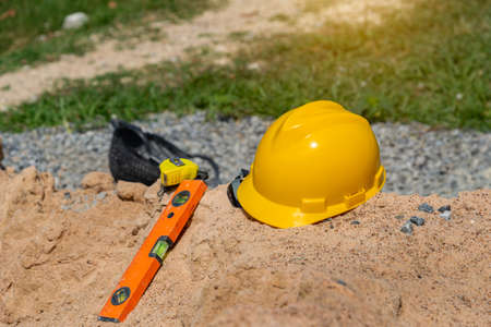 Yellow helmet on sand in construction site, Hard hat blueprint building construction estate project...