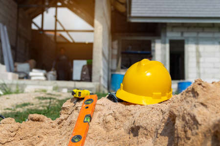 Yellow helmet on sand in construction site, Hard hat blueprint building construction estate project development.の写真素材