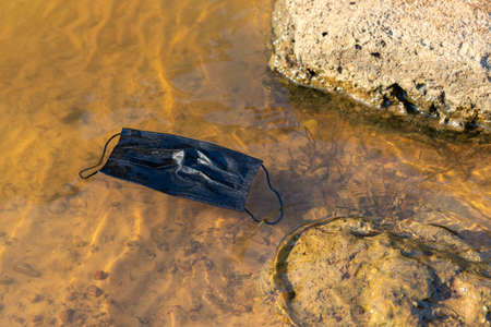 Coronavirus Plastic Waste Polluting the Environment. Discarded used disposable medical mask floats in reservoirの写真素材