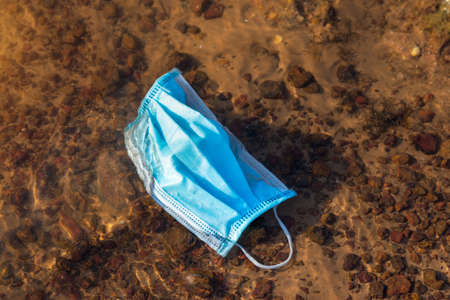 Coronavirus Plastic Waste Polluting the Environment. Discarded used disposable medical mask floats in reservoirの写真素材