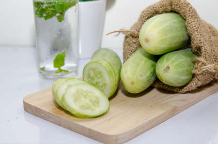 Heap of ripe cucumbers in jute bag on old white wooden table in garden on sunny day, healthy nutritionの写真素材