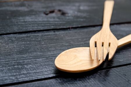 Handcrafted wooden kitchen utensils with a fork and spoons on a black wood の写真素材