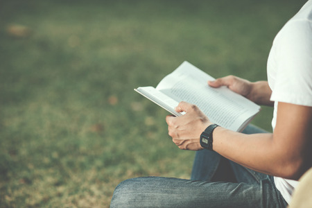 Close up Hansome man sitting on green grass reading book in summer