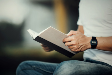 Close up Hansome man sitting on green grass reading book in summerの写真素材