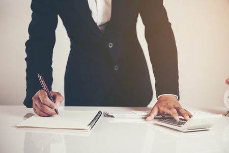 businessman working at laptop and writing in notebook in modern officeの写真素材