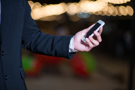 Close up businessman in suit using modern smart phone at night city in the blurred background with bokeh light, male hands holding tablet and phoneの写真素材