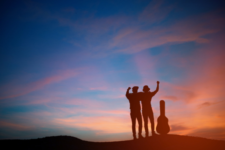 Silhouette of asia young two man with acoustic guitar, sunset backgroundの写真素材