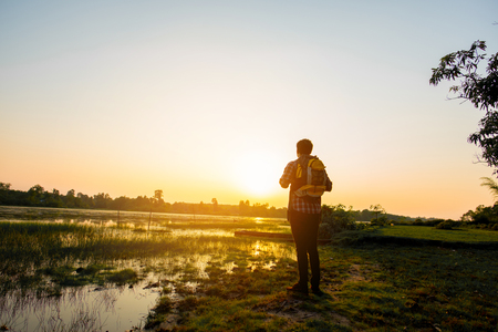 Hipster young man with backpack enjoying sunset on . Tourist traveler on background grass. Hiker looking sunlight in trip in thailand country, copy spaceの写真素材