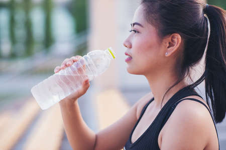 young woman drinking water after jogging