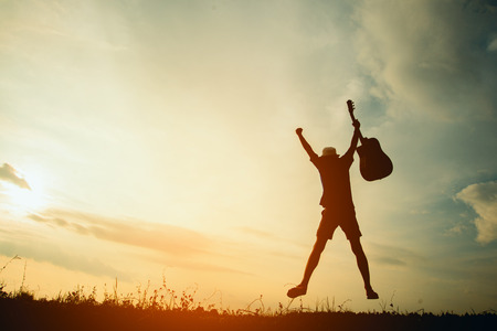 Silhouette fo musician holding acoustic guitar at the sky sunset, happy time in holiday, vintage toneの写真素材