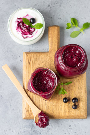Jar of delicious homemade black currant curd, custard or jam with natural yogurt and fresh berries on gray concrete background. Healthy breakfast.の写真素材